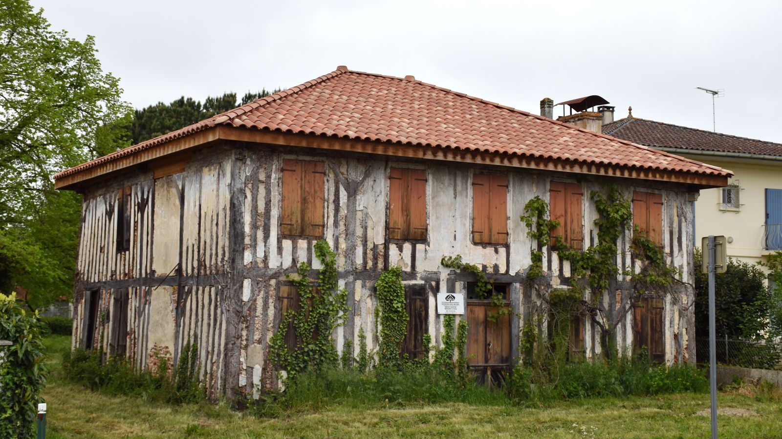 Maison à colombages abandonnée, volets clos, envahie par le lierre