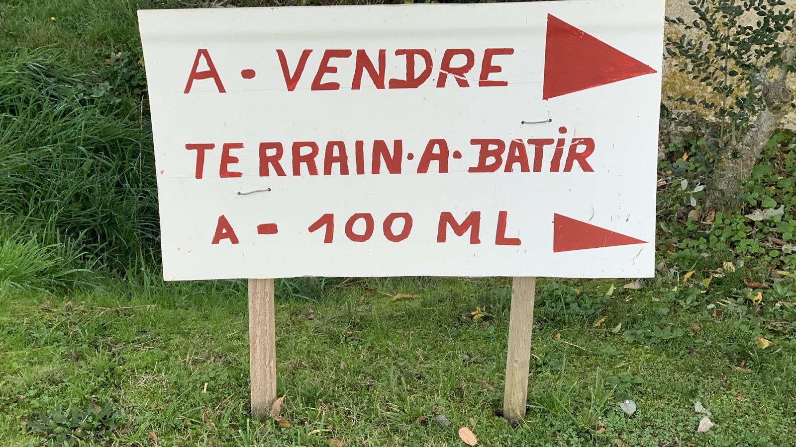 Panneau manuscrit « À vendre, terrain à bâtir » planté dans l'herbe