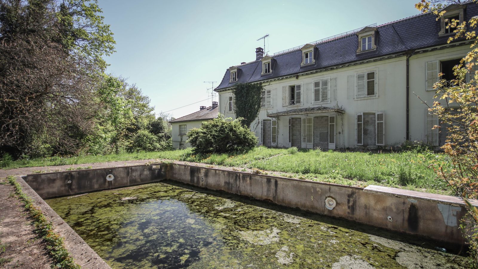 Large abandoned mansion with an algae-covered pond