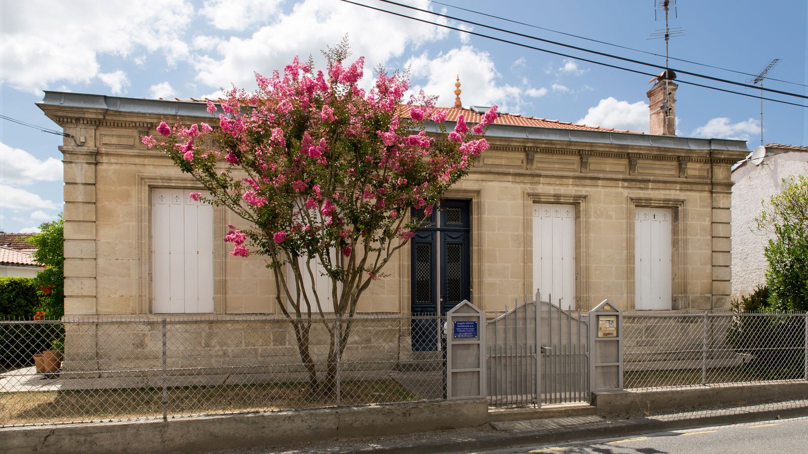 Maison basse en pierre avec un lilas des Indes en fleurs