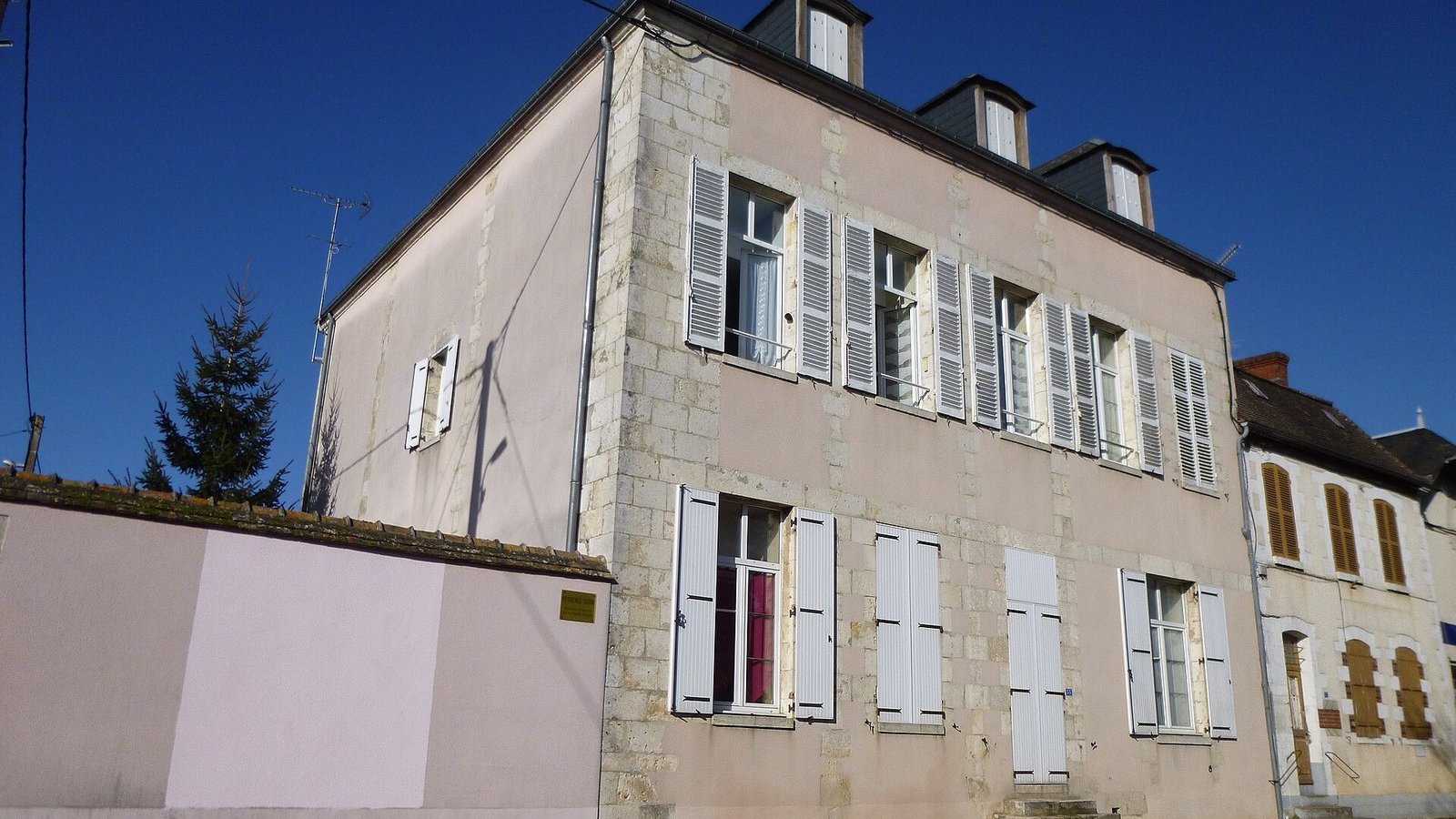 Maison de bourg en pierre aux volets blancs, sous un ciel bleu