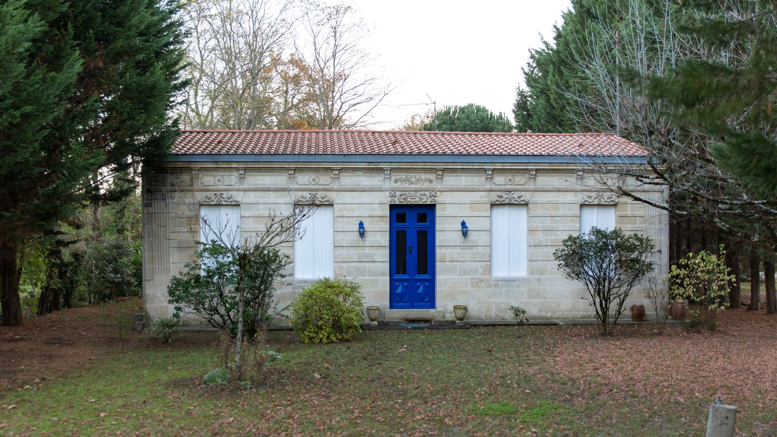 Maison basse en pierre aux volets fermés, devant une pelouse