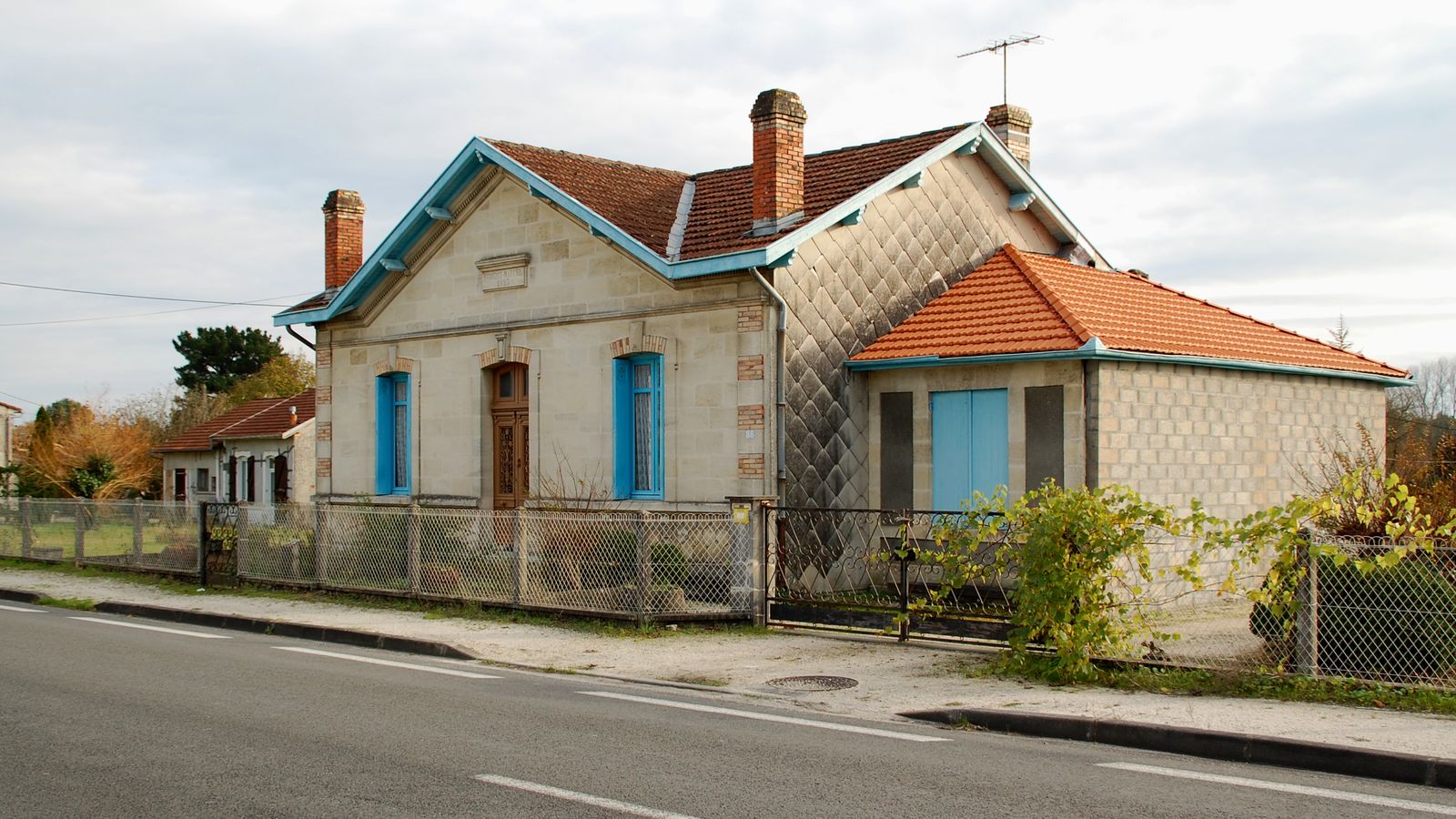Maison des années 1930 aux volets bleus, au bord d'une route