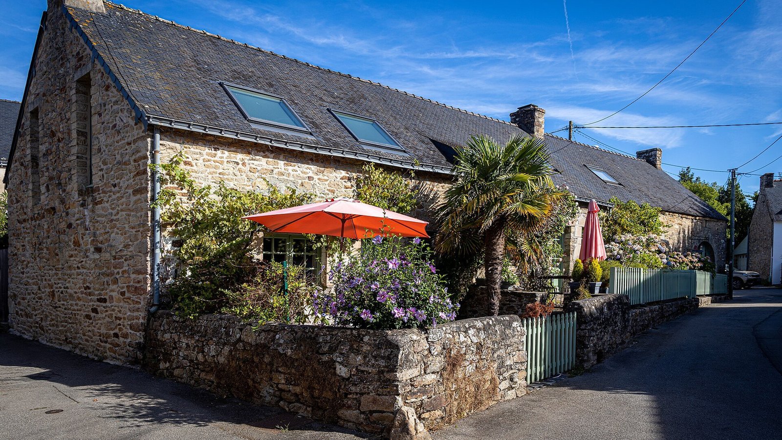 Maison en pierre fleurie avec un parasol orange, sous le ciel bleu