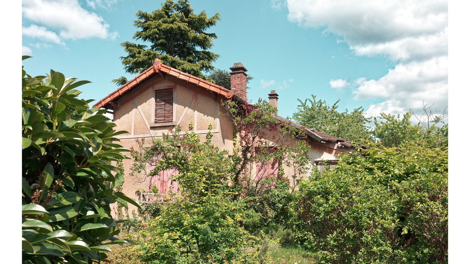 Maison à colombages roses cachée par une végétation abondante