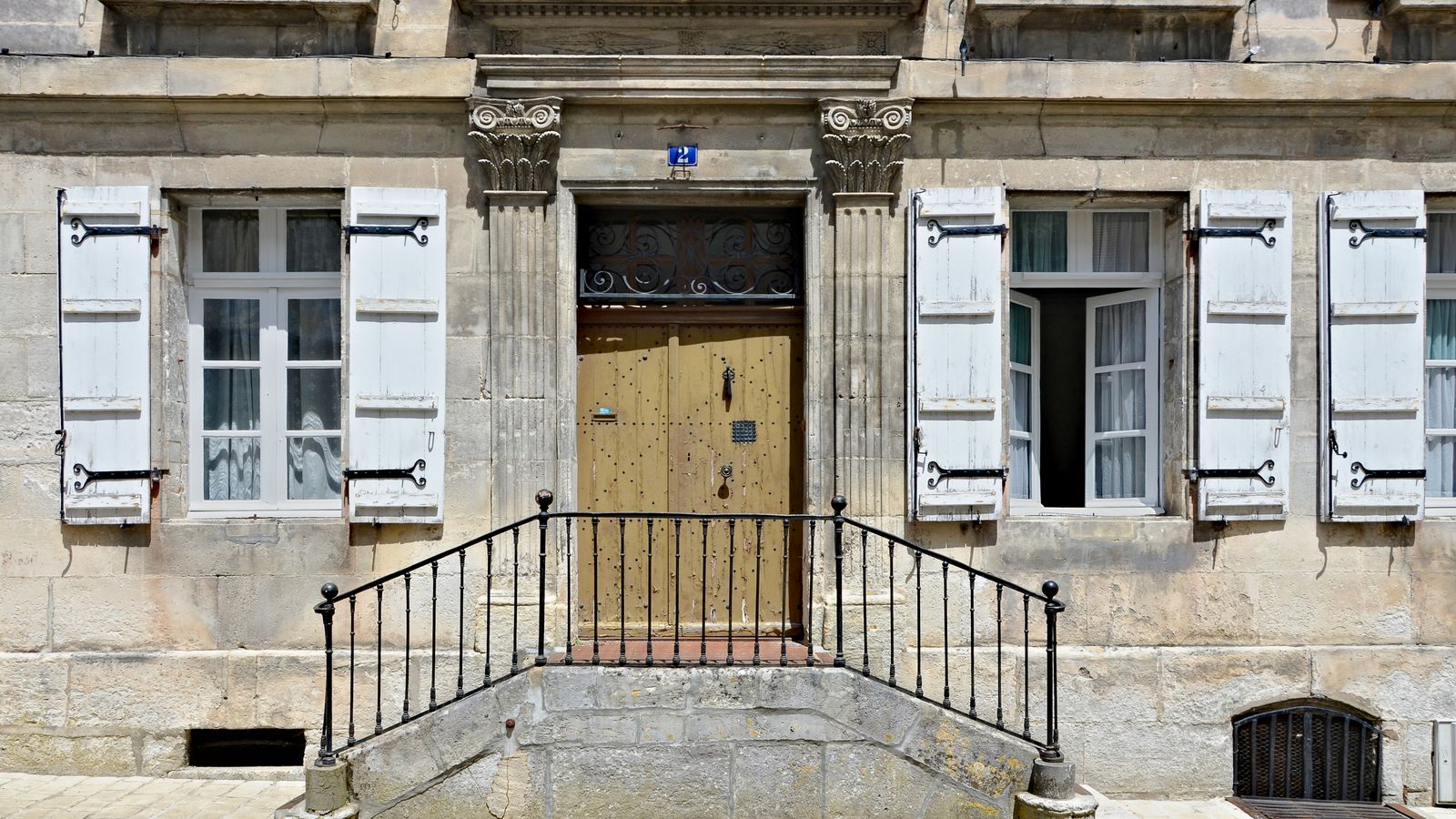 Façade de maison en pierre aux volets ouverts et porte en bois