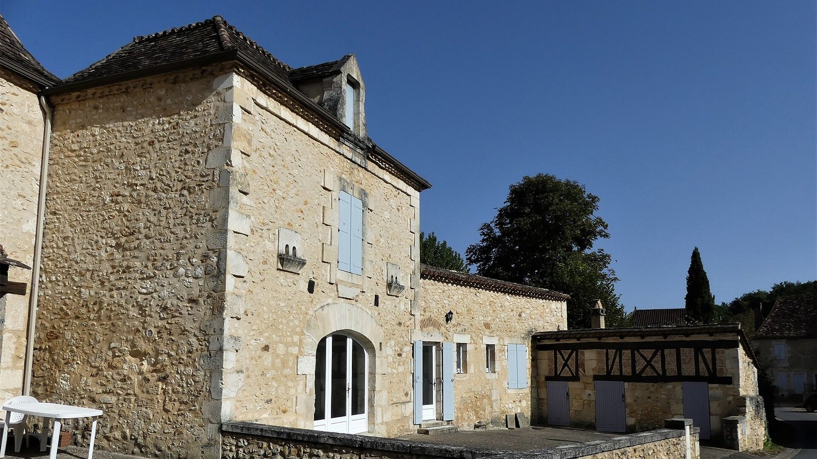 Stone house with blue shutters and its courtyard under a blue sky